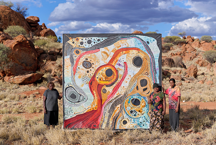 Pauline Minmila Wangin, Pitjantjatjara people, Betty Tjulpukuna Campbell, Pitjantjatjara people, and Emma Singer, Pitjantjatjara people, in Mimili, South Australia, 2022 with their work Kapi (Water), 2022